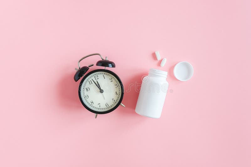 Zwei Pillen, weiße Flasche und schwarzer Wecker auf rosa Unterlage Schlafstörungen, Zeit bis zur Einnahme von Tabletten und lizenzfreies stockfoto Zwei Pillen, weiße Flasche und schwarzer Wecker auf rosa Unterlage Schlafstörungen, Zeit bis zur Einnahme von Tabletten und lizenzfreies stockfoto