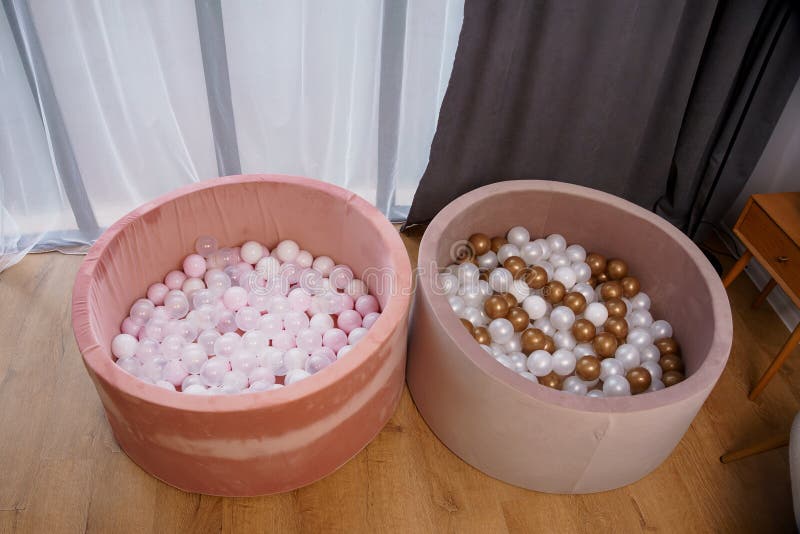 Zwei runde, rosa und beige weiche Ball-Pits, gefüllt mit rosa weißem Gold und durchsichtige Plastikbälle in der Nähe von Vorhängen lizenzfreie stockfotos