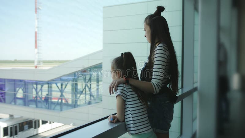 Zwei Schwestern stehen am Fenster des Warteraums des Flughafens mit Blick auf das Flugzeug