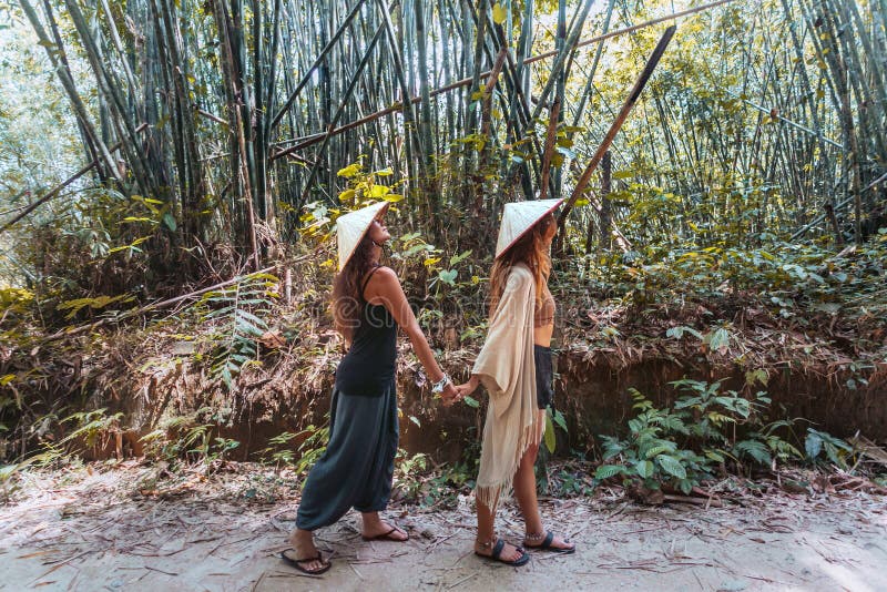 Zwei schöne junge Frau in asiatischen Hüten, die im Bambuswald spazieren