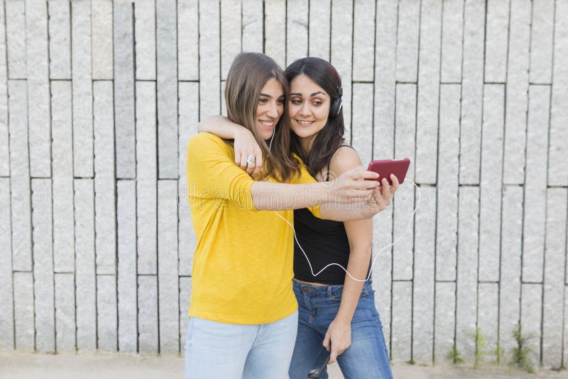 Zwei schöne junge Frauen, die Spaß draußen haben Machen eines Fotos mit Handy und Hören Musik Beiläufige Kleidung stadt stockbilder Zwei schöne junge Frauen, die Spaß draußen haben Machen eines Fotos mit Handy und Hören Musik Beiläufige Kleidung stadt stockbilder