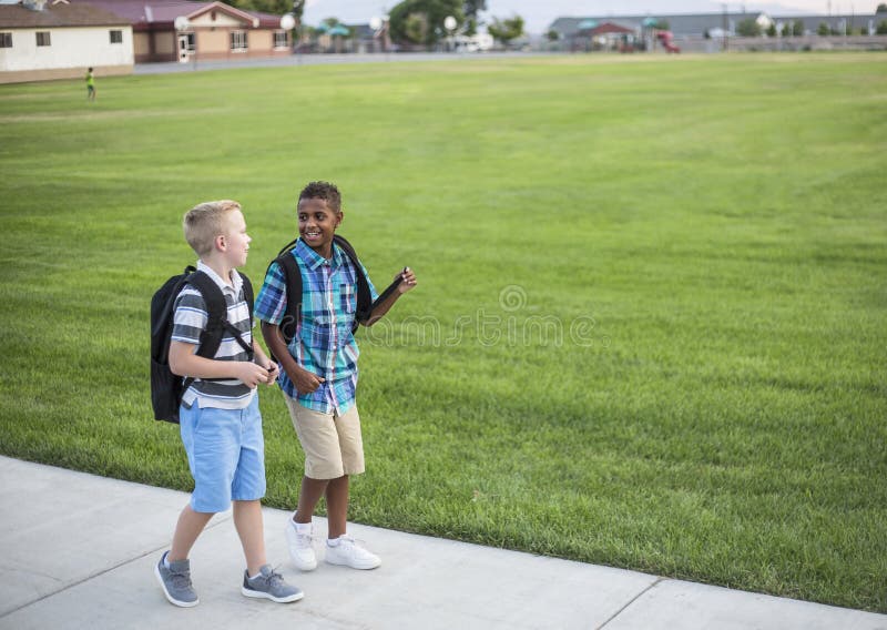 Zwei verschiedene Schulkinder nach Hause zusammen gehend nach der Schule stockfotografie Zwei verschiedene Schulkinder nach Hause zusammen gehend nach der Schule stockfotografie