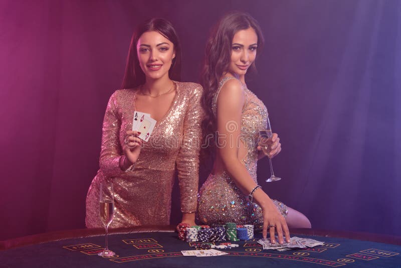 Zwei wunderschöne Frauen zeigen Karten beim Spielen am Tisch im Casino Schwarz, raucher Hintergrund mit farbenfrohen Farben stockfoto Zwei wunderschöne Frauen zeigen Karten beim Spielen am Tisch im Casino Schwarz, raucher Hintergrund mit farbenfrohen Farben stockfoto