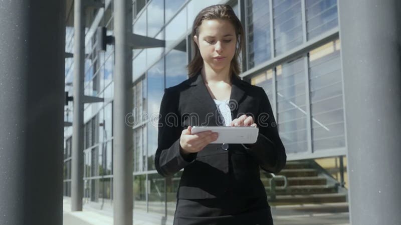 Zwolnione tempo młodego bizneswomanu pastylki chodzący pracujący komputer osobisty na zewnątrz zwolnionego tempa