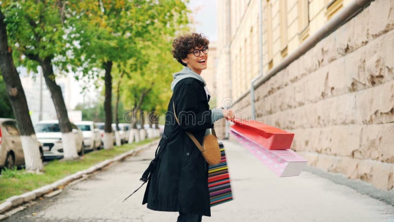 Zwolnione tempo portret uradowani z włosami dziewczyny mienia torba na zakupy i kręcenie wokoło z szczęśliwy śmiechu cieszyć się