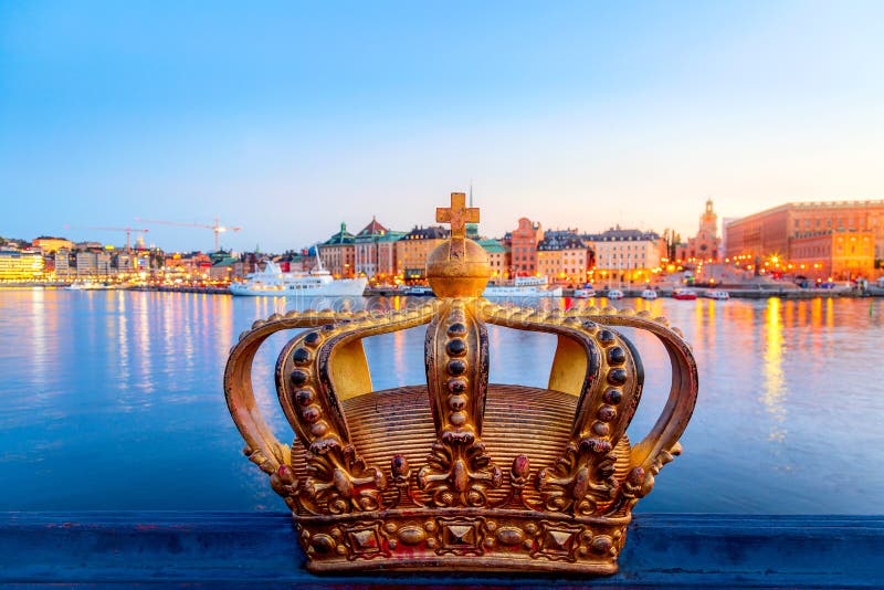 Złota korona na moście Skeppsholm z oświetlonym centrum sztokholmskim Gamla Stan w tle podczas zmierzchu słońca zdjęcie royalty free Złota korona na moście Skeppsholm z oświetlonym centrum sztokholmskim Gamla Stan w tle podczas zmierzchu słońca zdjęcie royalty free