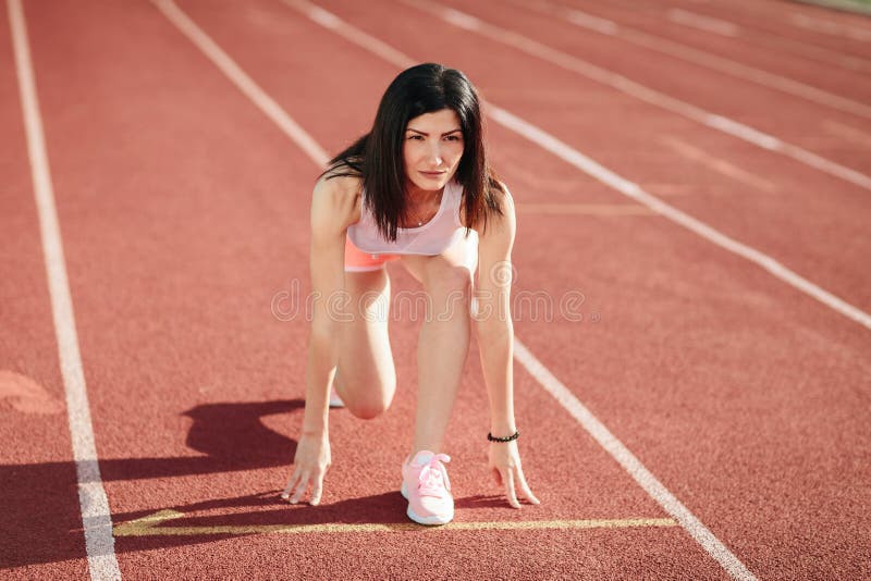 ¡Aliste para ir! Atleta de sexo femenino en pantalones cortos y camisetas sin mangas en la línea de salida de una pista del estad imagen de archivo ¡Aliste para ir! Atleta de sexo femenino en pantalones cortos y camisetas sin mangas en la línea de salida de una pista del estad imagen de archivo