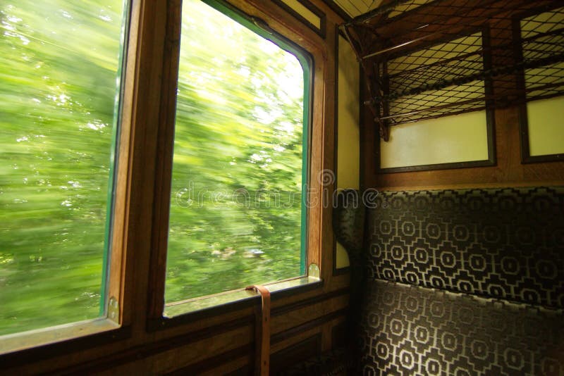 Picture of wooden interior of a steam train moving inside of a green forest. Picture of wooden interior of a steam train moving inside of a green forest