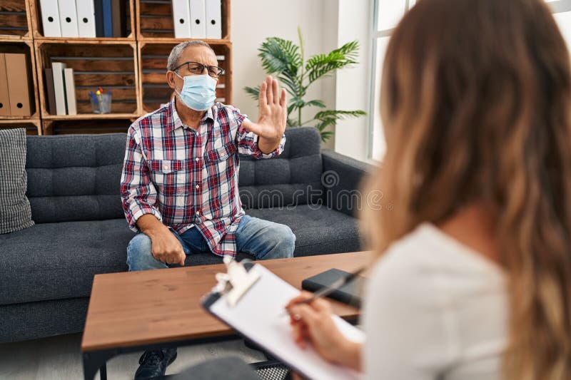 à la clinique de psychologie homme âgé dans le masque médical soulève la main avec défiance dans le signe grave face avec confianc photos stock