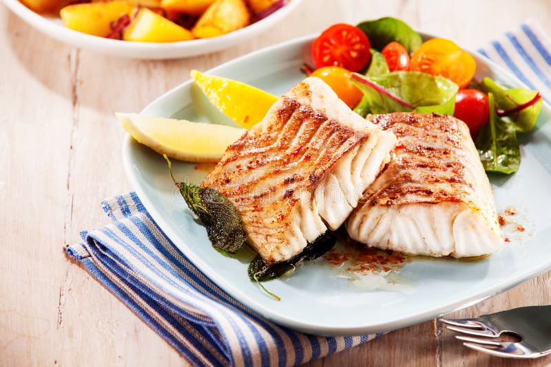 To portions of fresh grilled pollock or coalfish served with colorful salad and slices of lemon, close up high angle view. To portions of fresh grilled pollock or coalfish served with colorful salad and slices of lemon, close up high angle view