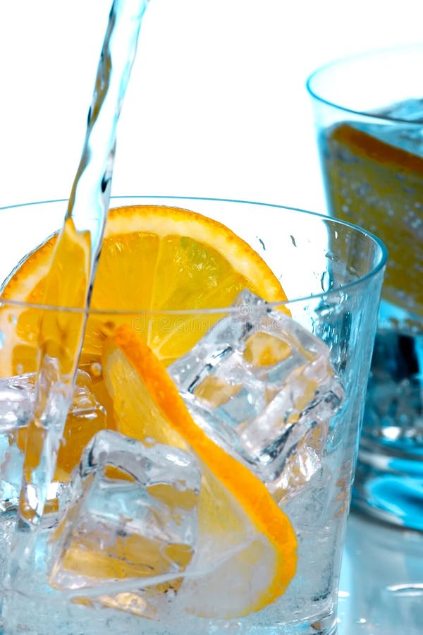 Pouring fresh water into one of two glasses with water, sliced lemon and ice cubes over aqua paper background. Pouring fresh water into one of two glasses with water, sliced lemon and ice cubes over aqua paper background