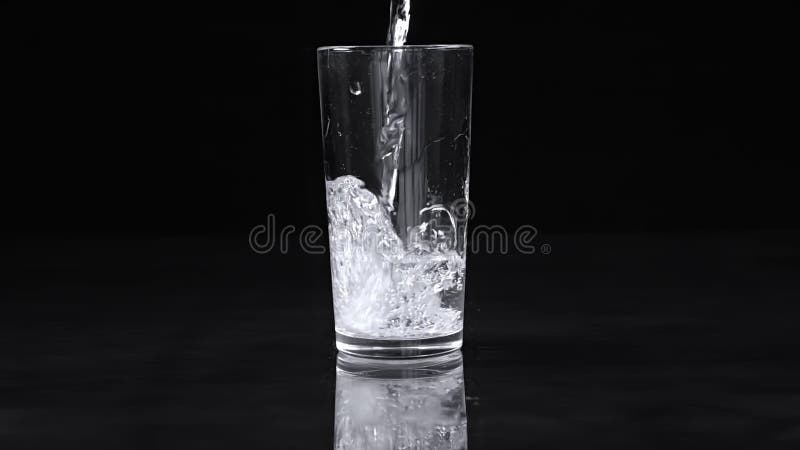 água despeja num copo com manchas sobre fundo preto. movimento lento