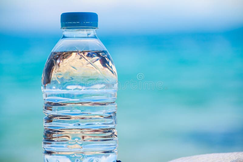 Água engarrafada em um dia quente na praia Garrafa plástica com água clara a beber, no fundo do mar garrafa da água sobre imagens de stock royalty free Água engarrafada em um dia quente na praia Garrafa plástica com água clara a beber, no fundo do mar garrafa da água sobre imagens de stock royalty free