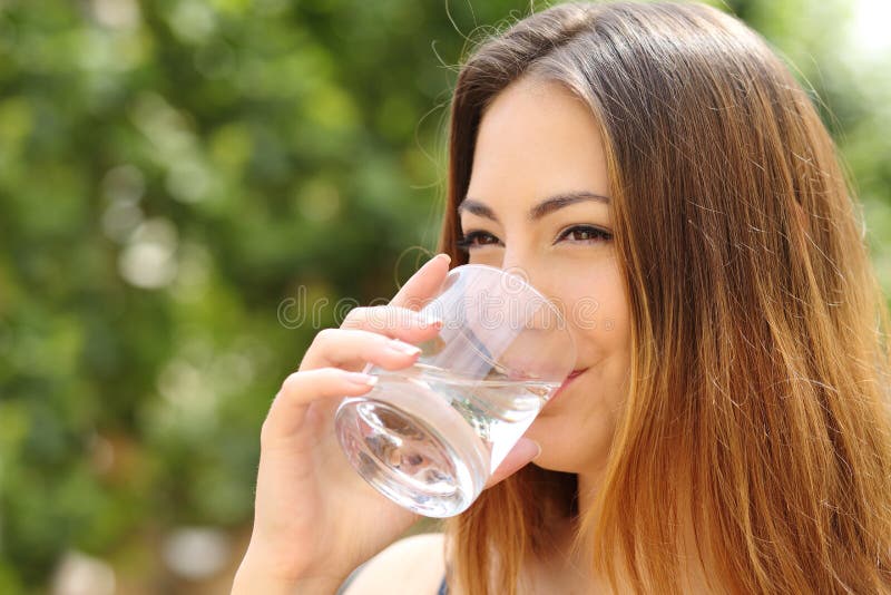 Água potável feliz da mulher de um vidro exterior