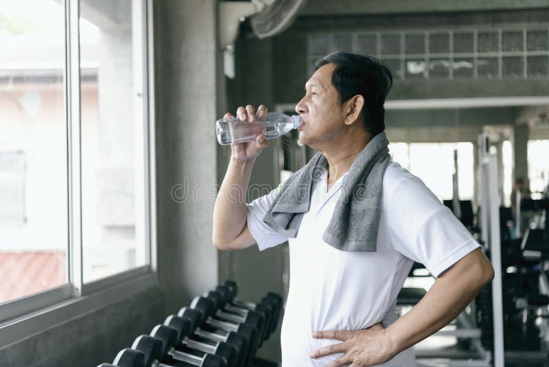 Água potável sedento asiática do homem superior após o exercício nos fitnes fotos de stock Água potável sedento asiática do homem superior após o exercício nos fitnes fotos de stock