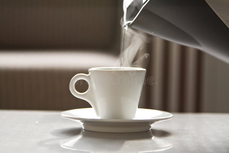 Água quente que flui de um teapot em um copo branco
