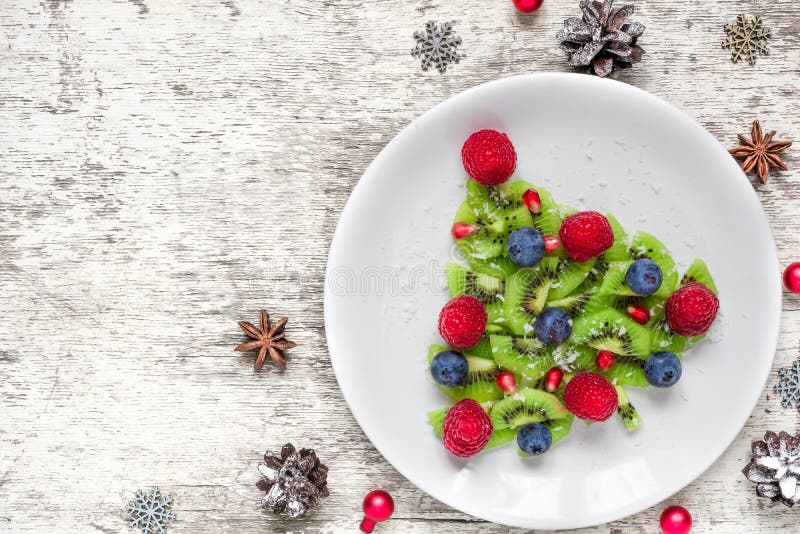 Árbol de navidad del kiwi con las bayas y el coco con los conos del pino sobre la tabla de madera blanca idea divertida de la com imagen de archivo libre de regalías Árbol de navidad del kiwi con las bayas y el coco con los conos del pino sobre la tabla de madera blanca idea divertida de la com imagen de archivo libre de regalías