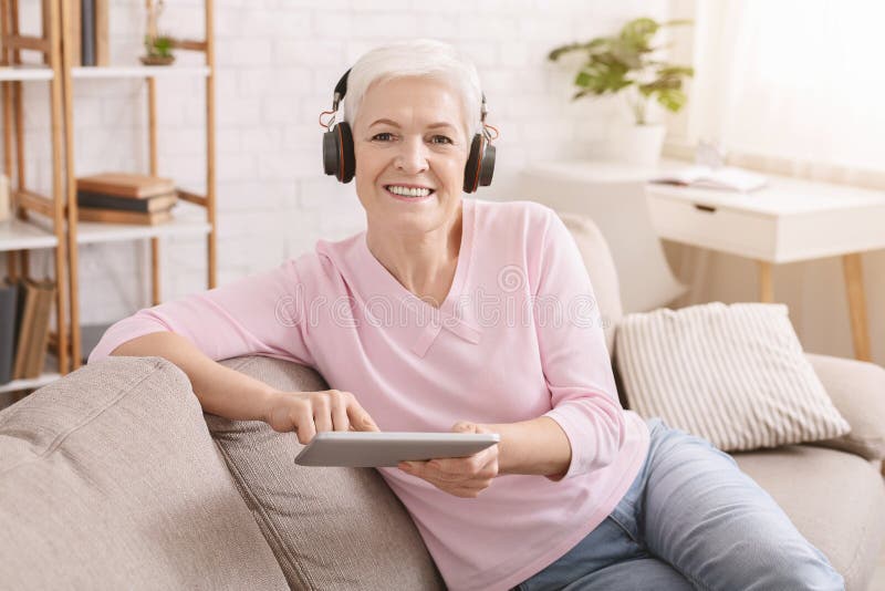 Senior woman enjoying music and watching videos on tablet pc in headphones, free space. Senior woman enjoying music and watching videos on tablet pc in headphones, free space