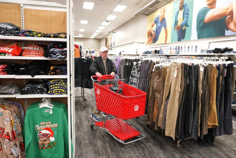 4 November 2023. Mt. Kisco, Westchester County, New York State. Bright red rolling basket glides over carpeted section of clothing store with pants and shirts on hangers. Old guy with ball cap and black jacket and hearing aids supports himself by gripping the handle bar. 4 November 2023. Mt. Kisco, Westchester County, New York State. Bright red rolling basket glides over carpeted section of clothing store with pants and shirts on hangers. Old guy with ball cap and black jacket and hearing aids supports himself by gripping the handle bar