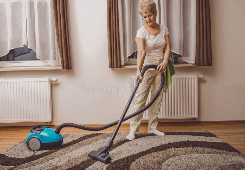 Elderly woman doing woman chores at home. Vacumming the carpet. Elderly woman doing woman chores at home. Vacumming the carpet.