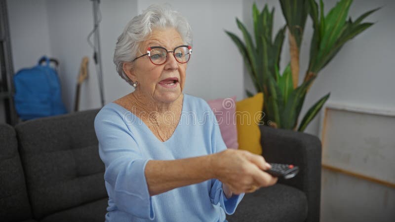 Äldre kvinna tittar bekvämt på TV i sitt moderna vardagsrum och har en avlägsen arkivbild