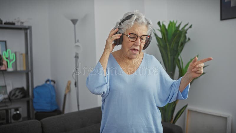 Äldre kvinnor lyssnar på musik med hörlurar i ett modernt vardagsrum som njuter och gester royaltyfria foton