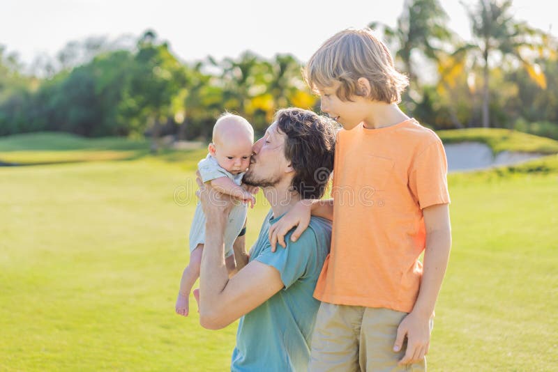 Äldre son och nyfödd barn på en ängsmark i parken. Familjeutgifter av hög kvalitet tillsammans i naturen. Parenthood fotografering för bildbyråer