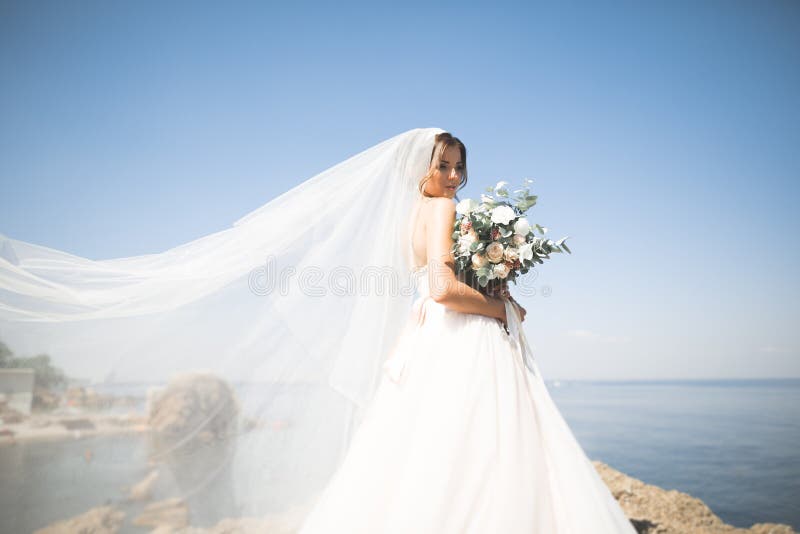 Älskvärd brud i den vita bröllopsklänningen som poserar nära havet med härlig bakgrund royaltyfri fotografi Älskvärd brud i den vita bröllopsklänningen som poserar nära havet med härlig bakgrund royaltyfri fotografi