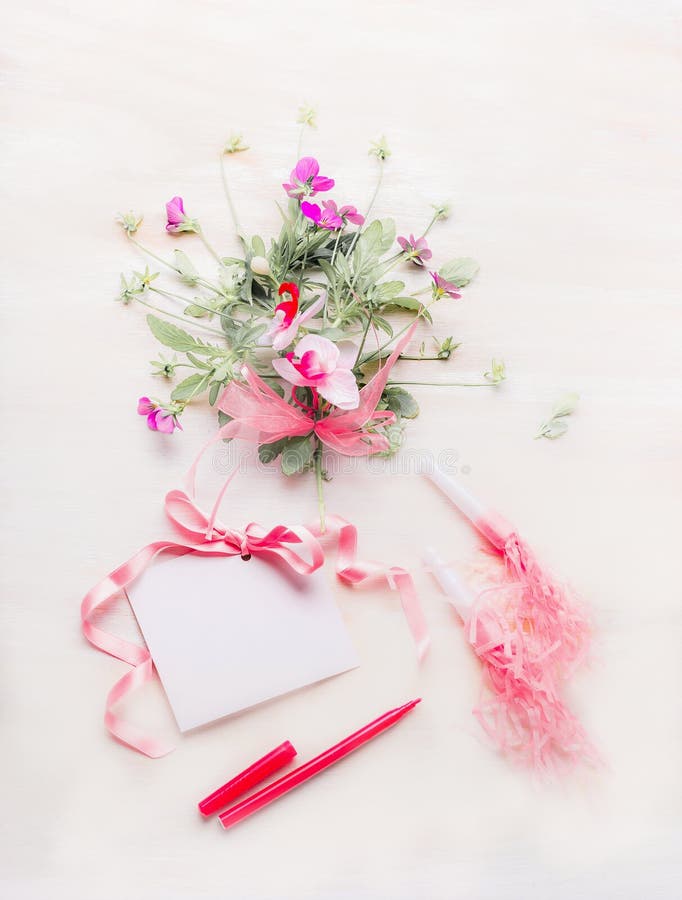 Älskvärda blommor samlar ihop och förbigår hälsningkortet med det rosa bandet och skriver eller markören på vit träbakgrund