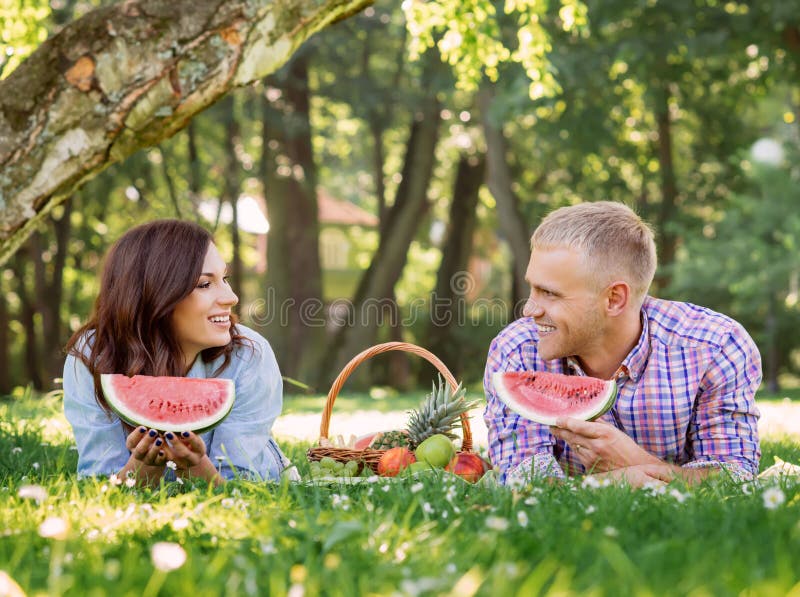 Älskvärda härliga par som äter vattenmelon och ligger på gräset i sommaren, parkerar royaltyfri bild