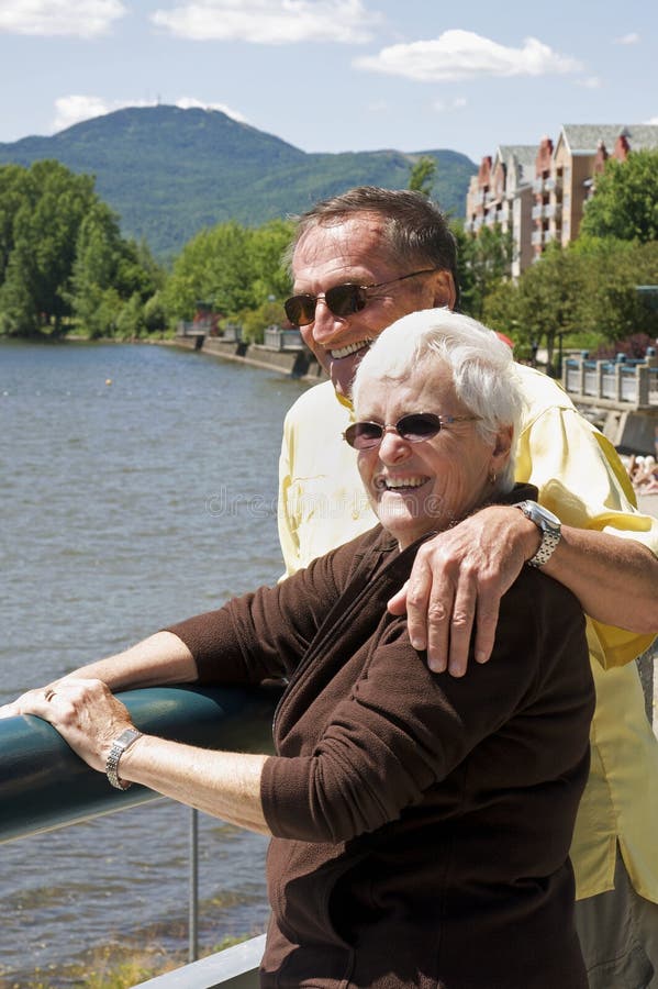 A handsome senior couple take in the sights at a lakeside resort in Magog, Quebec while on vacation. The peak in the background is Mont Orford, a popular ski destination. A handsome senior couple take in the sights at a lakeside resort in Magog, Quebec while on vacation. The peak in the background is Mont Orford, a popular ski destination.