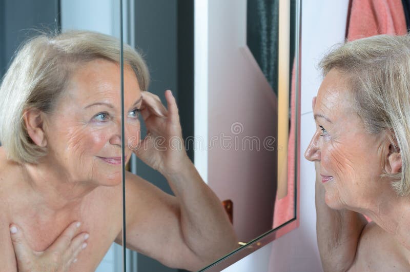 Ältere Dame, die ihre Haut im Spiegel überprüft stockbild Ältere Dame, die ihre Haut im Spiegel überprüft stockbild
