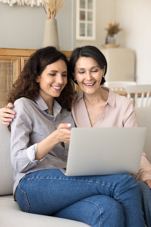 Ältere Mutter tausendjährige Tochter kuscheln auf Sofa entspannen mit Notebook lizenzfreies stockfoto