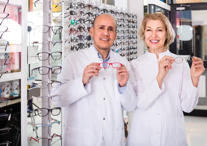 Happy elderly opticians helping to choose glasses in modern optics store. Happy elderly opticians helping to choose glasses in modern optics store