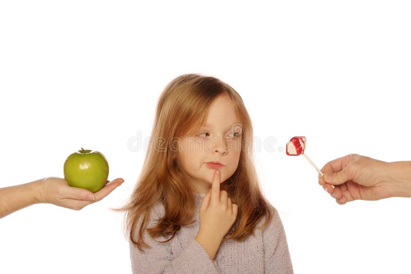 Young girl choosing between an apple and candy on an isolated background. Young girl choosing between an apple and candy on an isolated background