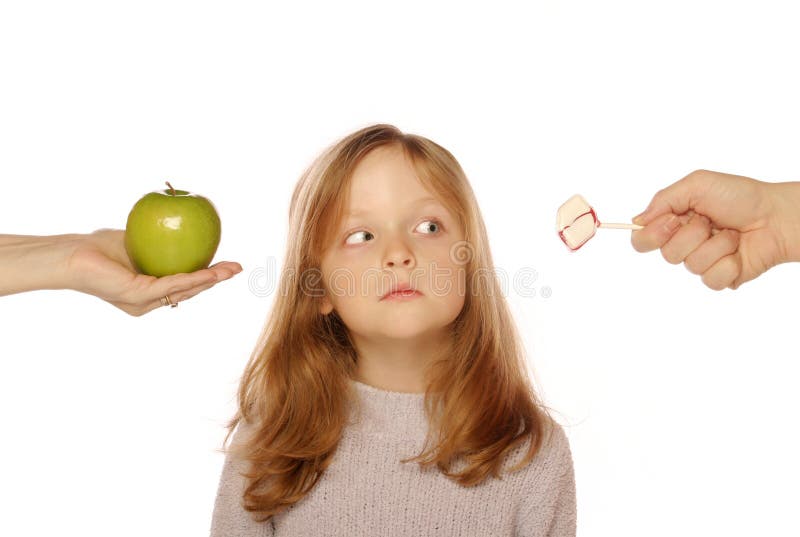 Young girl choosing between an apple and candy on an isolated background. Young girl choosing between an apple and candy on an isolated background