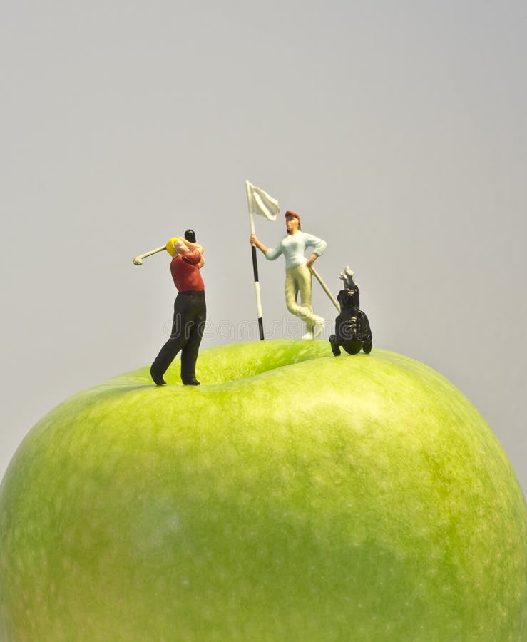 Macro shot of golfing figurines playing round on top of green apple. Macro shot of golfing figurines playing round on top of green apple