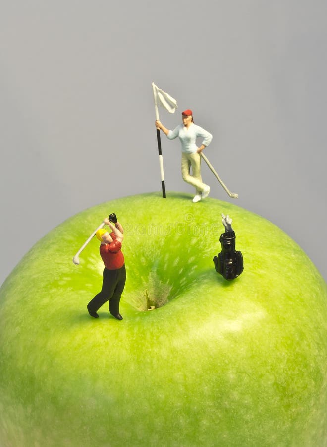 Macro shot of golfing figurines playing round on top of green apple. Macro shot of golfing figurines playing round on top of green apple