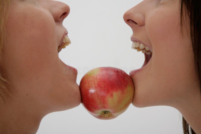 Two girls holdong red apple between chins, horizontal. Two girls holdong red apple between chins, horizontal