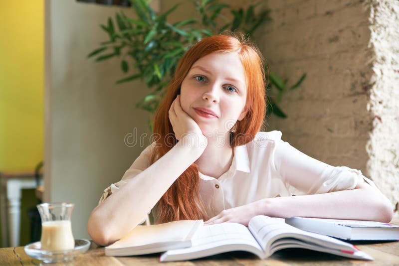 Är den kvinnliga studenten för den unga attraktiva flickan med vit hud och långt rött hår läseböcker och att studera som omger av arkivbilder Är den kvinnliga studenten för den unga attraktiva flickan med vit hud och långt rött hår läseböcker och att studera som omger av arkivbilder