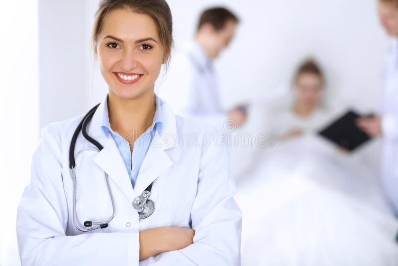Ärztin, die auf dem Hintergrund mit Patienten im Bett und zwei Doktoren lächelt lizenzfreies stockbild