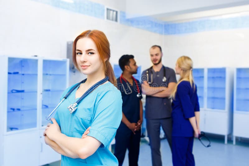Ärztin vor dem Team, Kamera mit Ärzteteam im Hintergrund betrachtend Gemischtrassiges Team von jungen Doktoren herein lizenzfreies stockbild Ärztin vor dem Team, Kamera mit Ärzteteam im Hintergrund betrachtend Gemischtrassiges Team von jungen Doktoren herein lizenzfreies stockbild