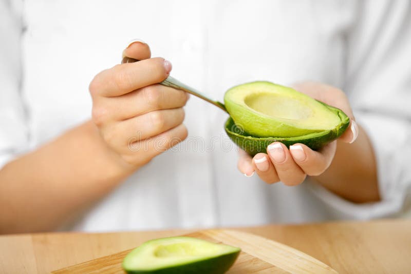 Eating Avocado. Woman Hands Peeling Fresh Avocado With Spoon. Close Up Of Female Hands Holding Organic Green Vegetable. Healthy Food. High Quality Image. Eating Avocado. Woman Hands Peeling Fresh Avocado With Spoon. Close Up Of Female Hands Holding Organic Green Vegetable. Healthy Food. High Quality Image.