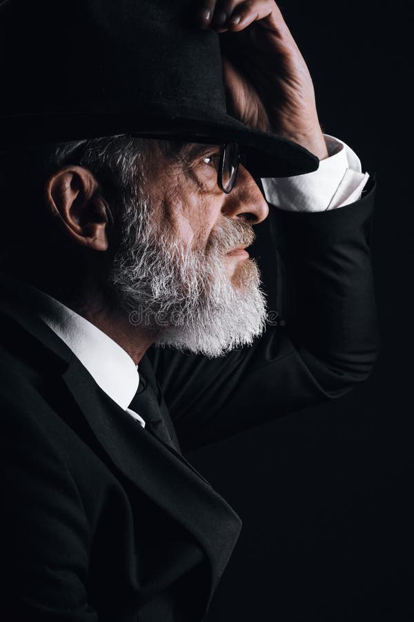 ålderdomlig man i bild av engelsk hemlig agent med hatt på ögonen mot mörk vägg royaltyfri foto