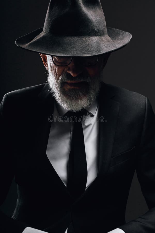 ålderdomlig man i bild av engelsk hemlig agent med hatt på ögonen mot mörk vägg fotografering för bildbyråer