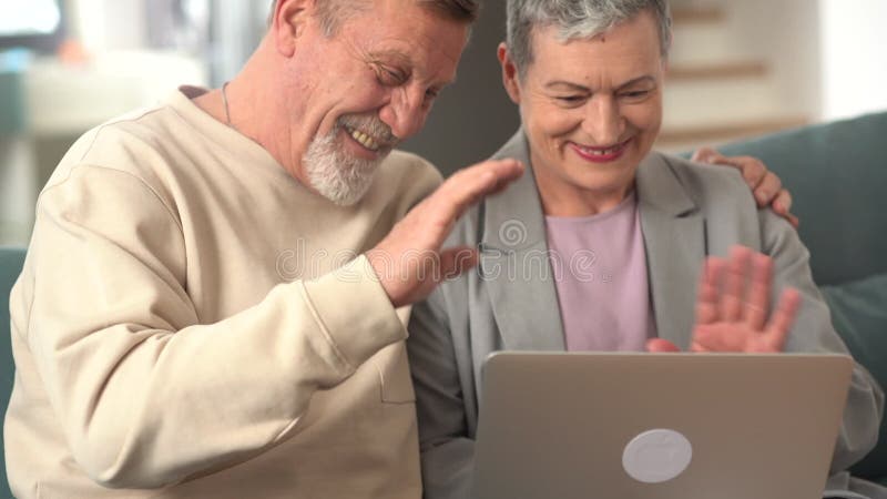 åldrat par som sitter på soffan och har videokonferens med sin familj på en bärbar dator. Internetkommunikation med barn
