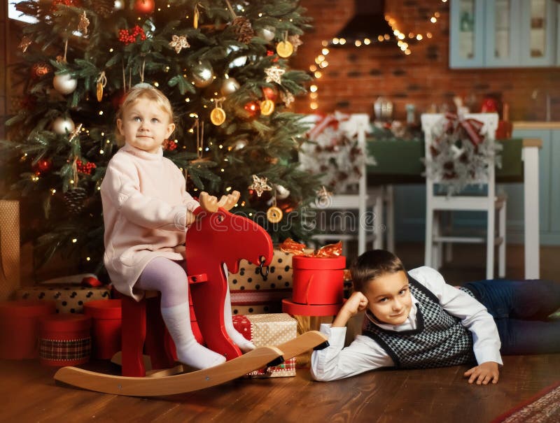 3 år gammal flicka i rosa klänning på röd rockhjort nära julgranen med julklapp och presentlådor runt omkring Pojken lägger på arkivbilder 3 år gammal flicka i rosa klänning på röd rockhjort nära julgranen med julklapp och presentlådor runt omkring Pojken lägger på arkivbilder
