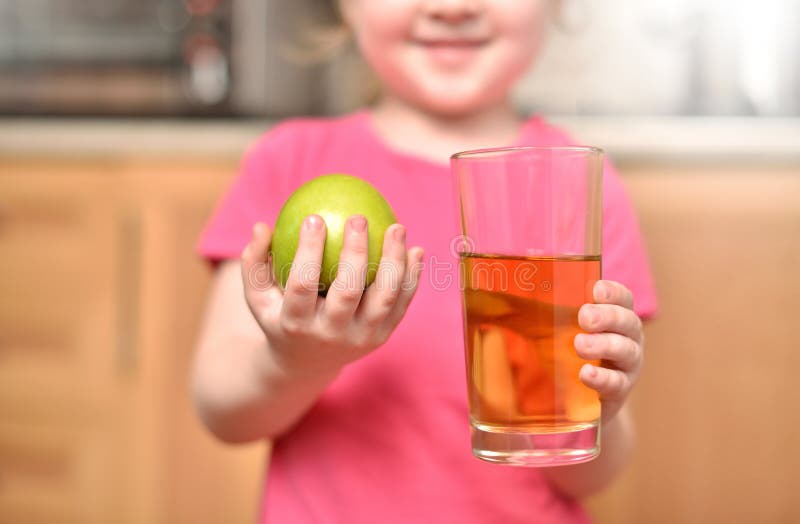 Girl child 4-6 years old smiling and holding a green apple and a glass with juice. Girl child 4-6 years old smiling and holding a green apple and a glass with juice