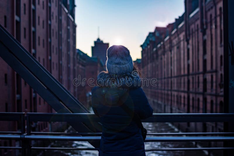 后面女孩景色 在观看现代大厦的桥梁的女孩身分日落和柔光 汉堡, Hafencity 免版税库存照片 后面女孩景色 在观看现代大厦的桥梁的女孩身分日落和柔光 汉堡, Hafencity 免版税库存照片