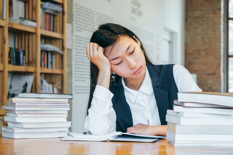 坐在图书馆里的逗人喜爱的亚裔女孩,包围由书,休息从学校 一名少年学生为检查,作为做准备 库存图片 坐在图书馆里的逗人喜爱的亚裔女孩,包围由书,休息从学校 一名少年学生为检查,作为做准备 库存图片